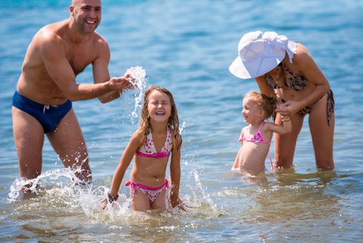 young happy couple with cute little daughters having fun while splashing each other in the shallow water of the sea during Summer vacation  Healthy family holiday concept