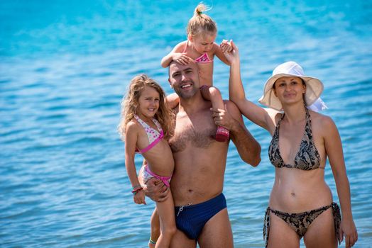 portrait of a young happy couple with cute little daughters having fun while standing in the shallow water of the sea during Summer vacation  Healthy family holiday concept