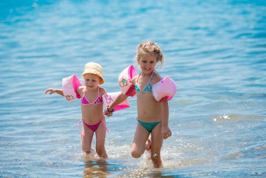 two happy little girls with swimming armbands playing in shallow water of the sea during Summer vacation  Healthy childhood lifestyle concept