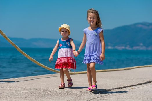 Happy smiling little sisters having fun holding their hands while walking on the beach coast during Summer vacation  Healthy childhood lifestyle concept