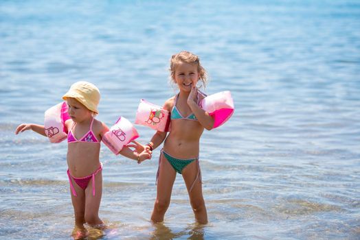 two happy little girls with swimming armbands playing in shallow water of the sea during Summer vacation  Healthy childhood lifestyle concept