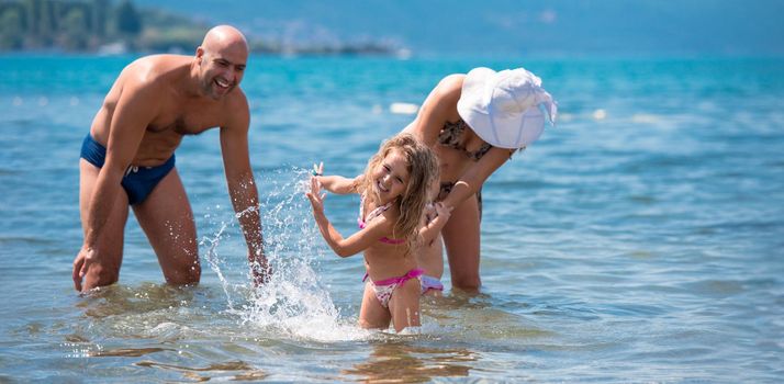 young happy couple with cute little daughters having fun while splashing each other in the shallow water of the sea during Summer vacation  Healthy family holiday concept