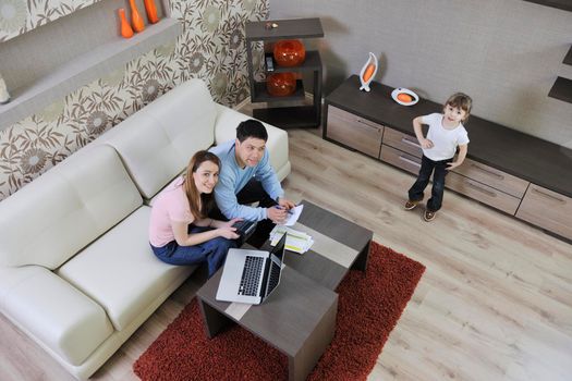 young happy family at bright and modern living room puting money in piggy bank and working on laptop computer on home finance