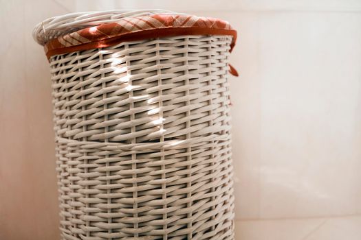 A white laundry basket, stylishly made of wicker wood, stands in the bathroom.