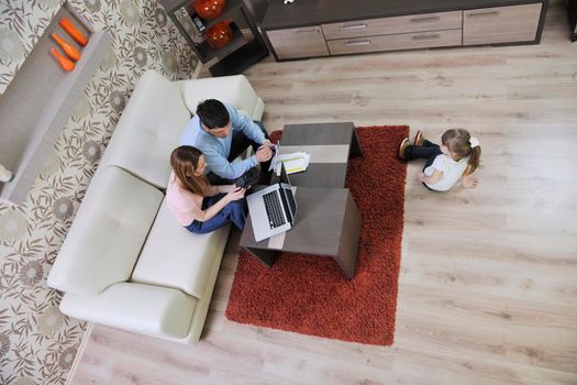 young happy family at bright and modern living room puting money in piggy bank and working on laptop computer on home finance