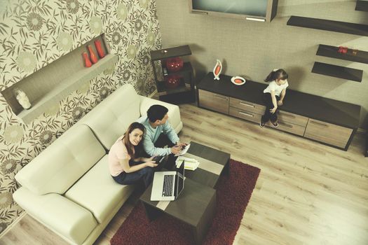 young happy family at bright and modern living room puting money in piggy bank and working on laptop computer on home finance