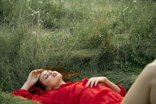 pretty woman in red dress lies on the grass freedom landscape. High quality photo