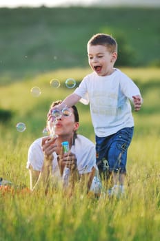 happy child and woman outdoor playing with soap bubble on meadow