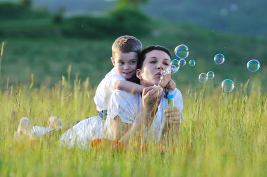 happy child and woman outdoor playing with soap bubble on meadow