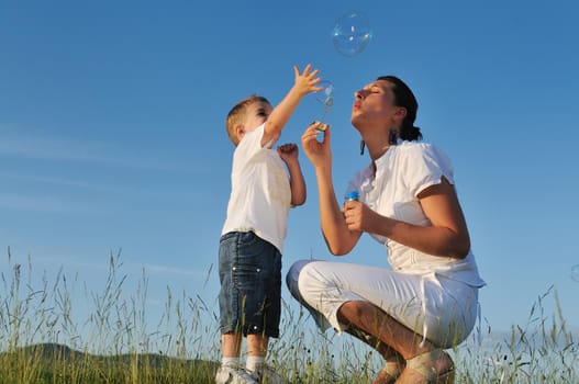 happy child and woman outdoor playing with soap bubble on meadow