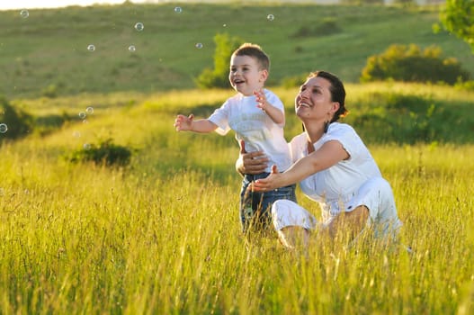 happy child and woman outdoor playing with soap bubble on meadow