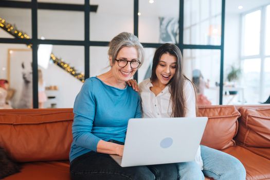 Mother and daughter sitting on couch and watching something on laptop at home