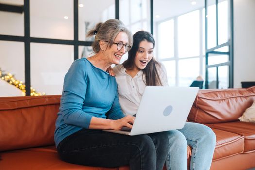 Mother and daughter sitting on couch and watching something on laptop at home