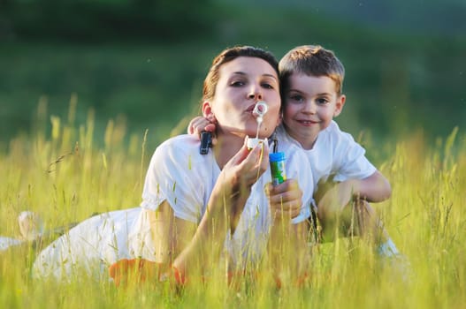 happy child and woman outdoor playing with soap bubble on meadow