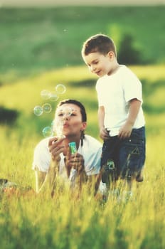 happy child and woman outdoor playing with soap bubble on meadow