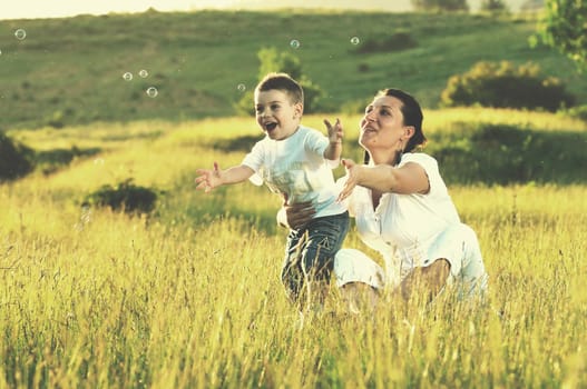 happy child and woman outdoor playing with soap bubble on meadow