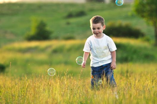 happy young beautiful child have fun on eadow with soap bubbles toy