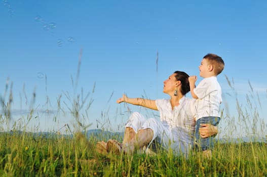 happy child and woman outdoor playing with soap bubble on meadow