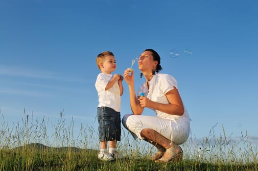happy child and woman outdoor playing with soap bubble on meadow