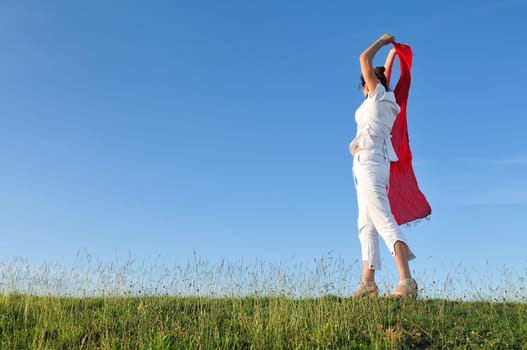 beautiful young and healthy woman run and jump on meadow at sunny day with red scarf