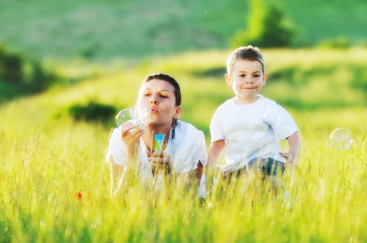 happy child and woman outdoor playing with soap bubble on meadow