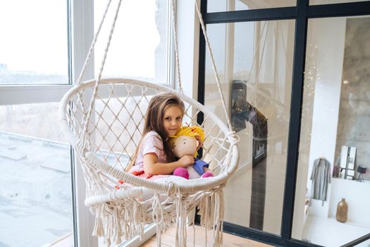 Little girl looks at camera sitting in white hanging chair