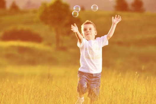 happy young beautiful child have fun on eadow with soap bubbles toy
