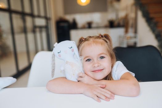 Little smiling girl hugging favorite toys while sitting at table happy childhood