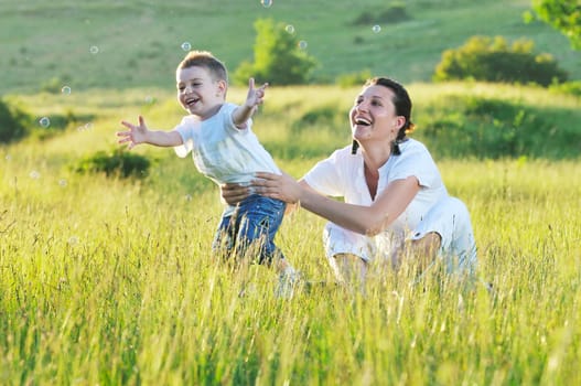 happy child and woman outdoor playing with soap bubble on meadow