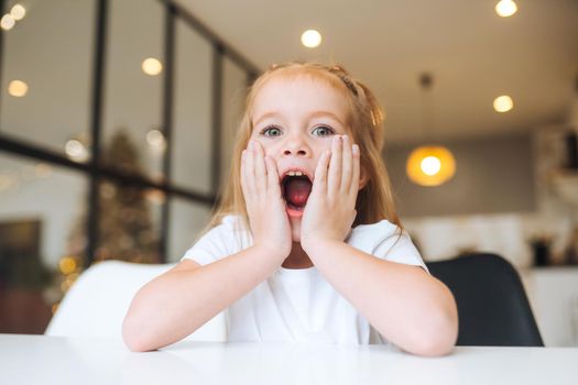 Portrait of a little surprised girl in a white dress at home