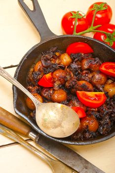 Baby cuttle fish roasted on iron skillet with tomatoes and onions over rustic wood table