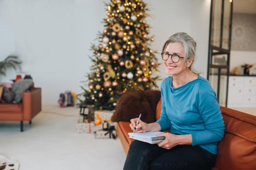 Grandma sits on the couch writing something in a note at home