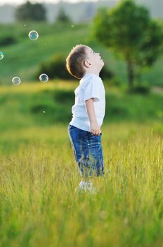 happy young beautiful child have fun on eadow with soap bubbles toy