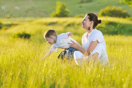 happy child and woman outdoor playing with soap bubble on meadow