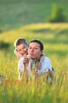 happy child and woman outdoor playing with soap bubble on meadow