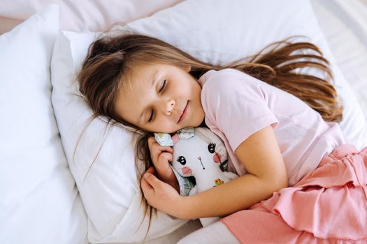 health and beauty concept - little girl with toy sleeping at home