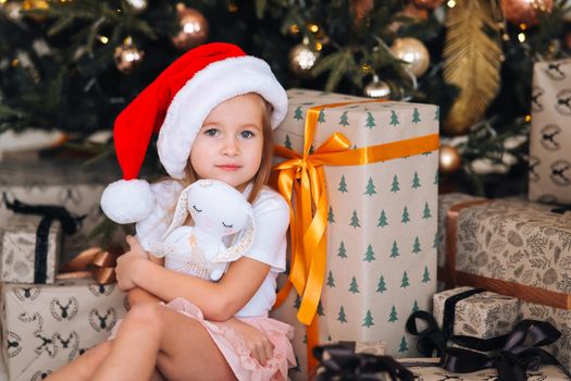 Happy little girl hugs her favorite toy in the room decorated for the New Year and Christmas