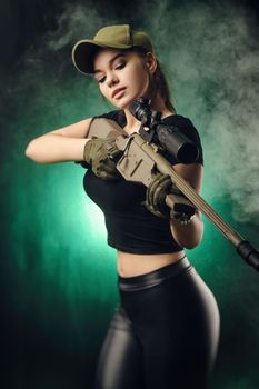 girl in military special clothes posing with a gun in his hands on a dark background in the haze