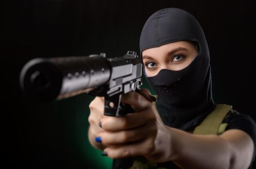 girl in military special clothes posing with a gun in his hands on a dark background in the haze