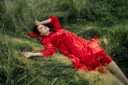 woman in red dress lies on the grass in the field nature landscape. High quality photo