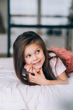 Beautiful little girl lying in the bed looking away.