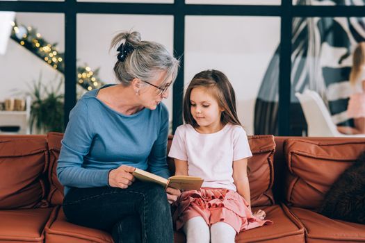 Nice elderly woman grandmother reading story to granddaughter. Happy family at home concept