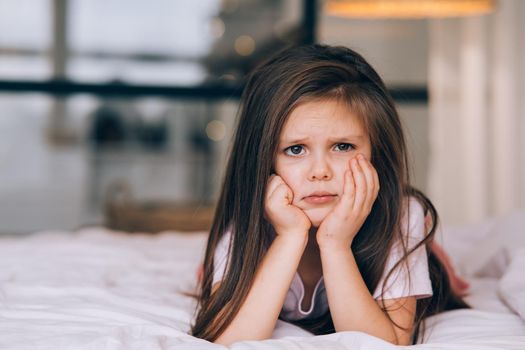 Cute little girl with a sad face lying on the bed. Children emotional concept.