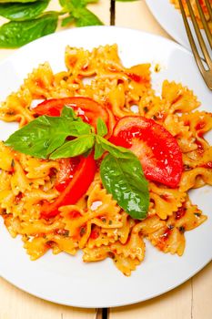 Italian pasta farfalle butterfly bow-tie with tomato basil sauce over white rustic wood table