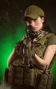 girl in military special clothes posing with a gun in his hands on a dark background in the haze