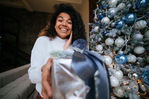 Woman gives a gift to his friend in the camera. Portrait of a young woman of Afro appearance ethnic, black curly hair brunette.