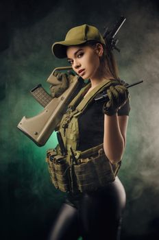 girl in military special clothes posing with a gun in his hands on a dark background in the haze