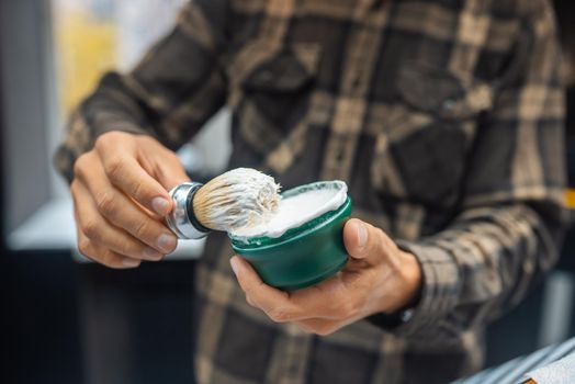 The master holds a brush and shaving foam in his hand at barbershop