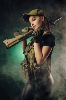 girl in military special clothes posing with a gun in his hands on a dark background in the haze