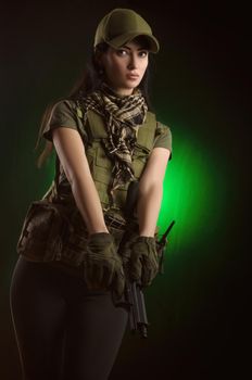 girl in military special clothes posing with a gun in his hands on a dark background in the haze